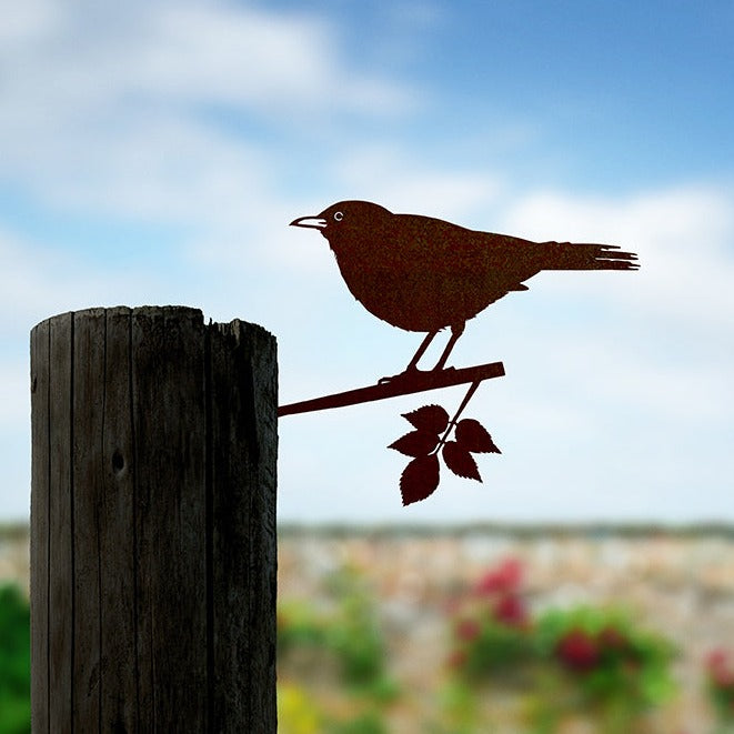 Steel Blackbird silhouette on a leafy branch installed in a wooden post in a garden.