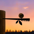 Silhouette of the Metalbird UK Stick Feeder, a metal bird feeder with seed ball on a wooden post, set against a sunset sky. "Metalbird" is cut into the metal—ideal as unique garden art or a thoughtful gift.
