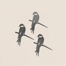 The Baby Bird Bundle - Swallow Trio by Metalbird UK features three stylized black-and-white swallows with white cheeks, perched on branches against a light beige background, evoking corten steel yard art in a loose triangular formation.