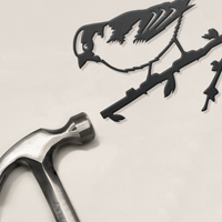 A premium metal hammer rests next to Metalbird UK's House Sparrow—a black, cut-out bird silhouette perched on a branch—set against a plain light background.